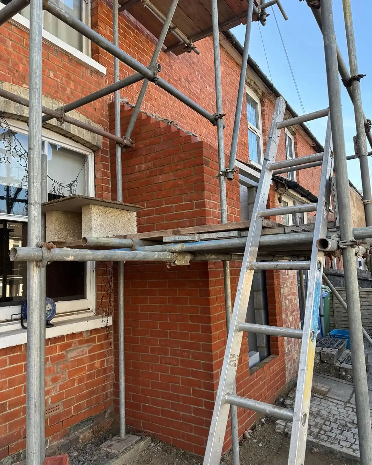 Scaffolding and ladder set up around a brick house with a new brick extension under construction.