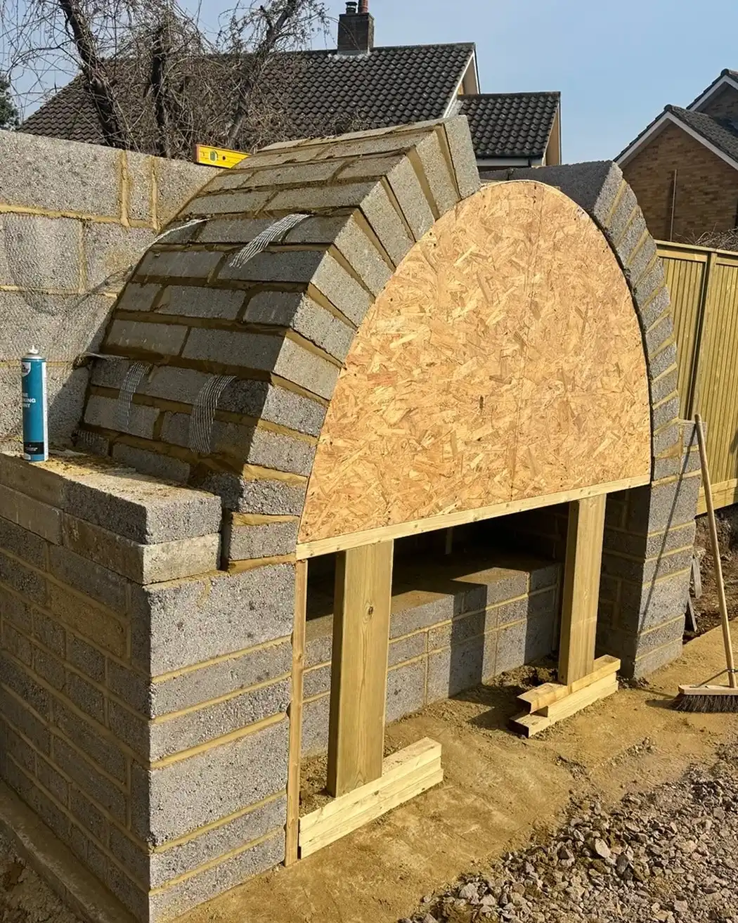 Partially built outdoor brick oven with arched top framed by wood on a dirt ground.
