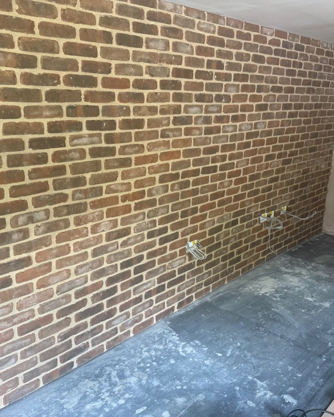 Interior room with a newly built brick wall and unfinished concrete floor with electrical wires exposed.