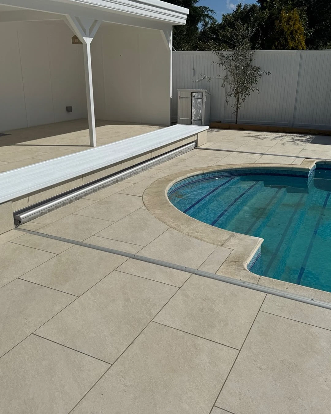 Outdoor pool with clear blue water next to a beige tiled patio and white shaded seating area.