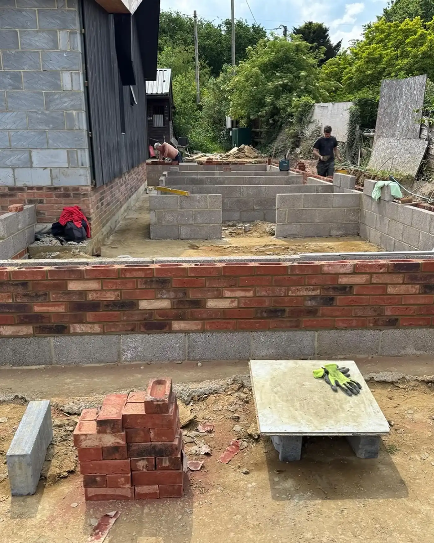 Construction site with brick and concrete block walls partially built and two workers laying bricks.