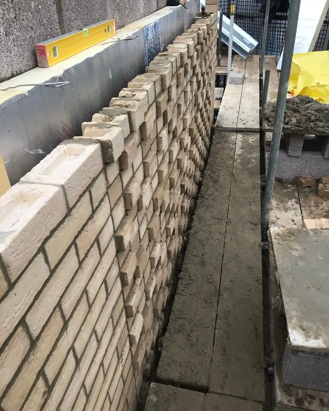 Construction of a brick wall with staggered bricks and wet mortar on wooden planks beside it.