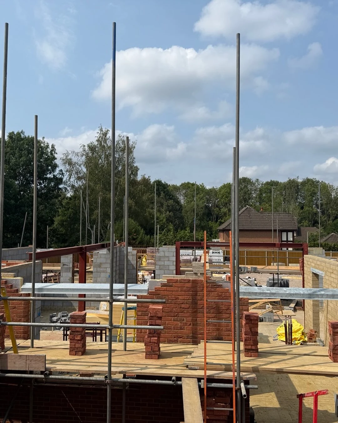 View of a residential building under construction with scaffolding and brick walls on a sunny day.