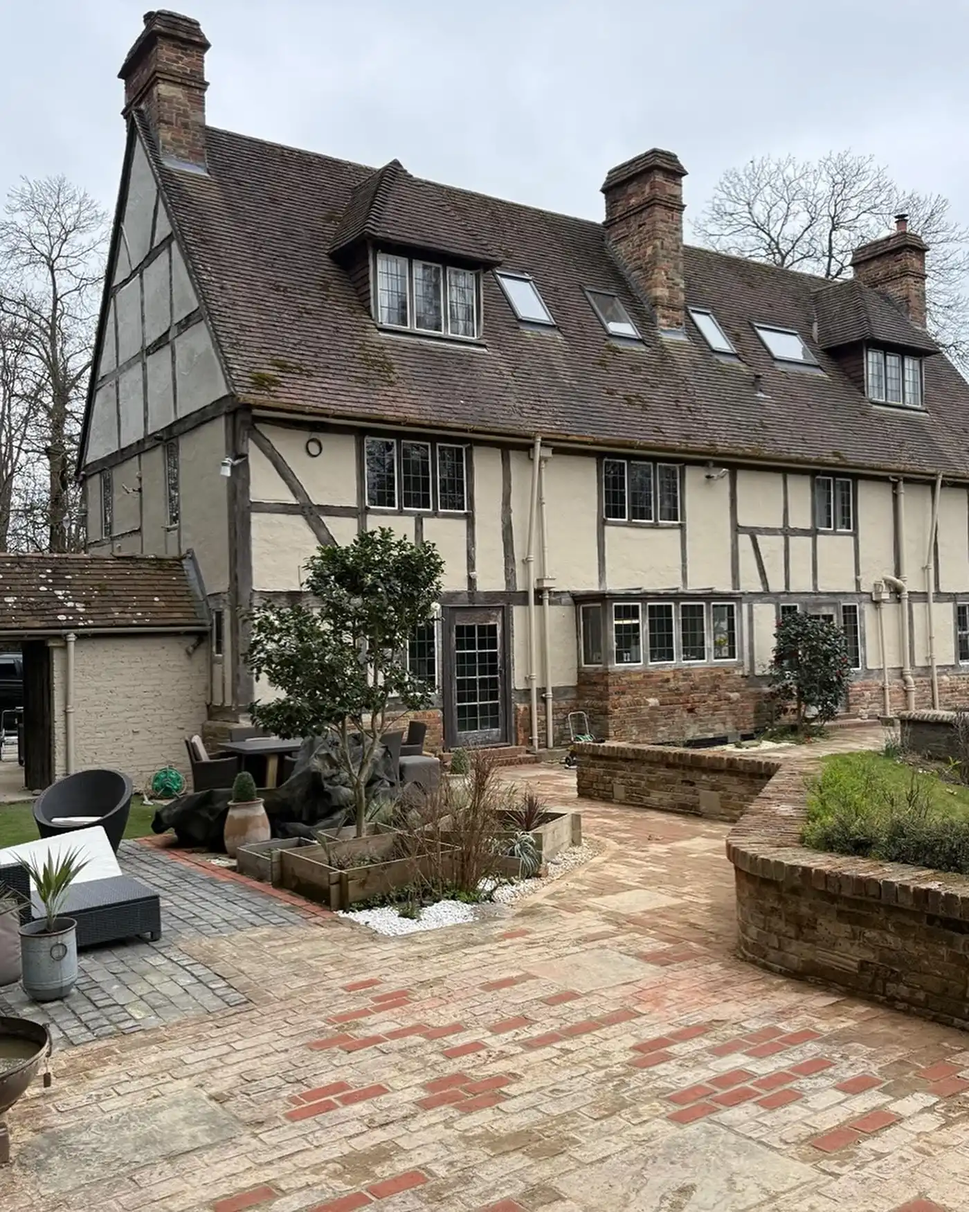 Large historic half-timbered house with multiple chimneys and a brick patio with plants and seating.