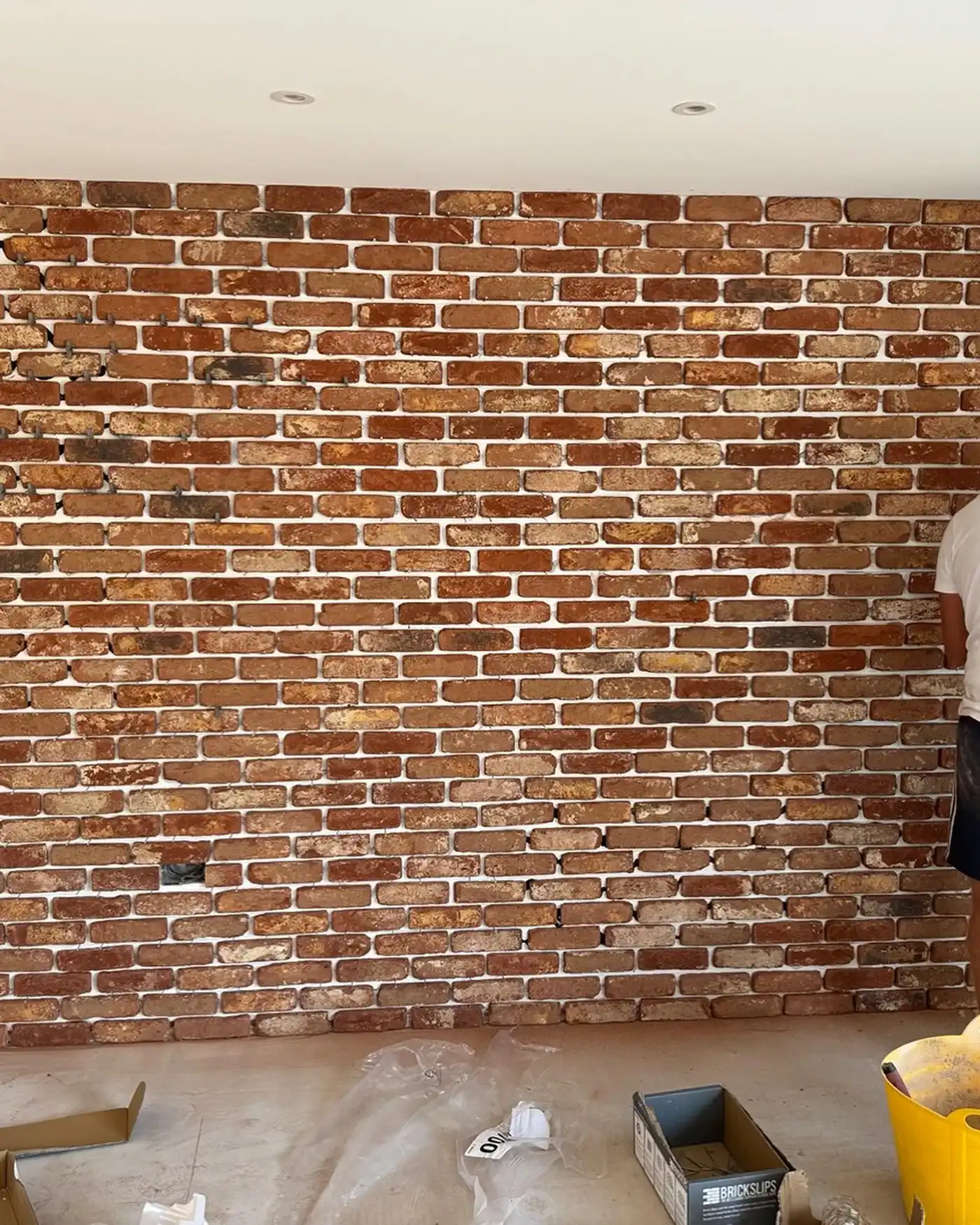 Partially finished interior brick wall with construction materials and person on right side.