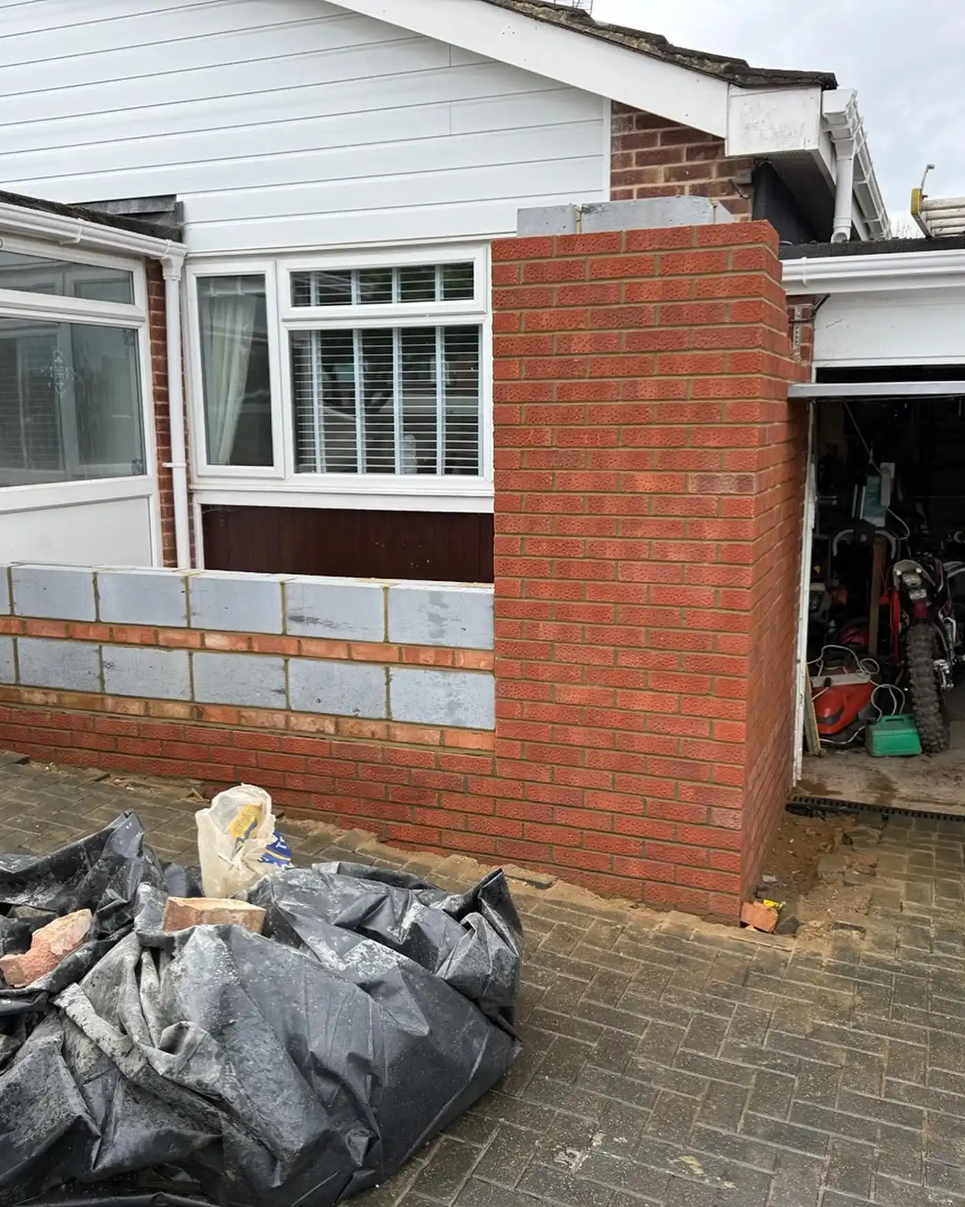 Construction site of a house extension brick wall with building materials and garage entrance visible.