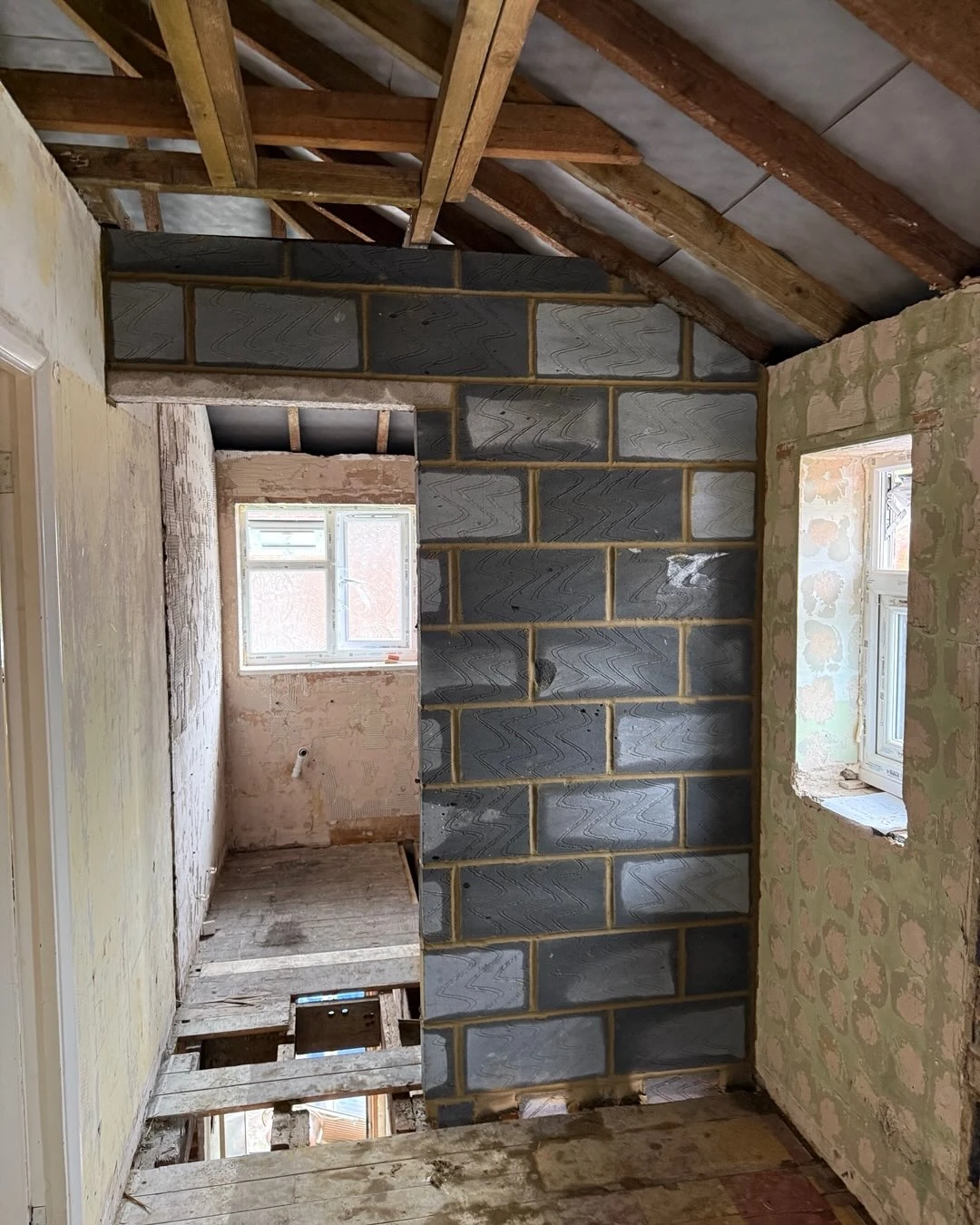 Interior of a room under renovation with exposed beams, a new block wall, and partially removed floorboards.