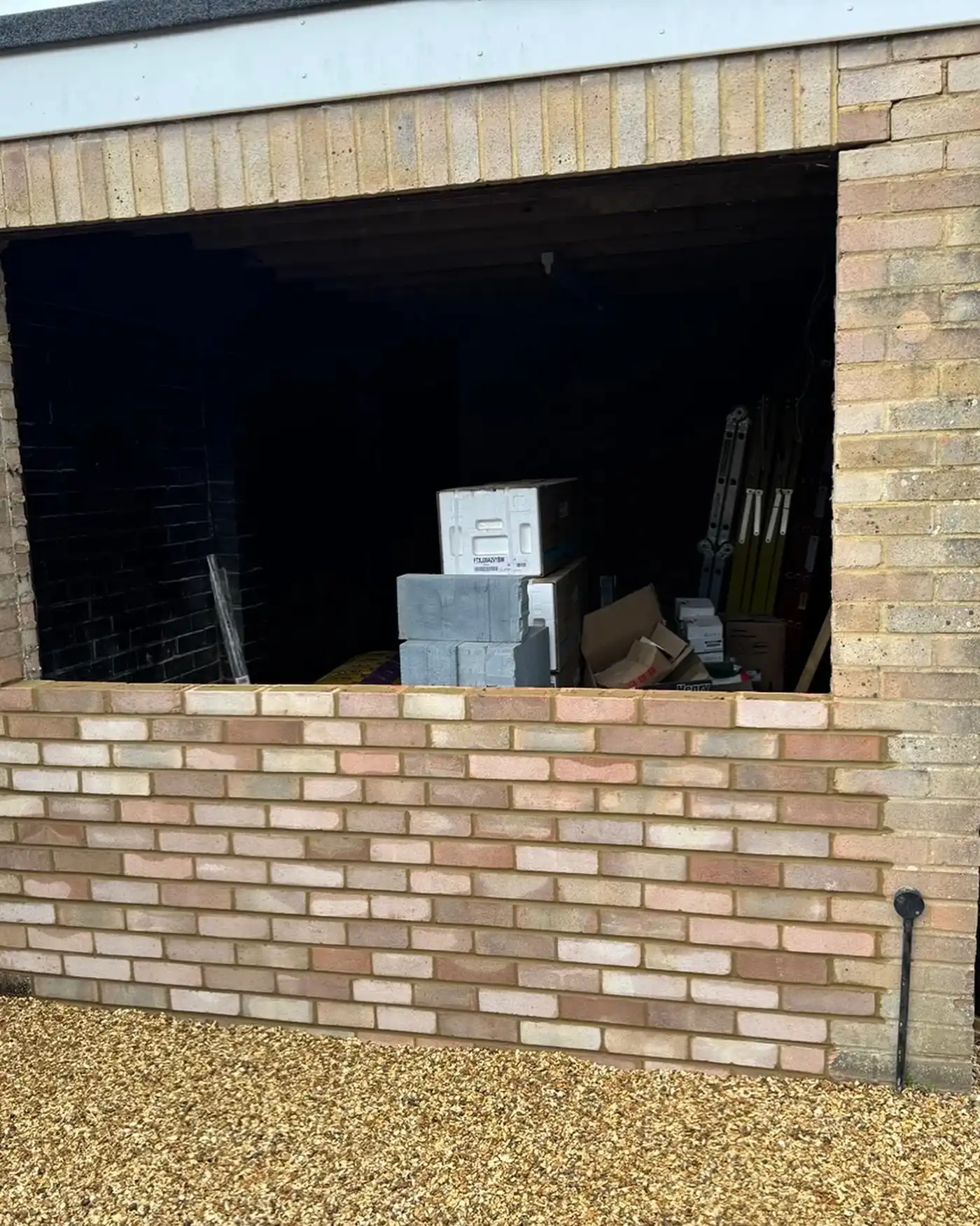 Partially built brick wall in front of a dark opening with stacked concrete blocks and boxes inside.