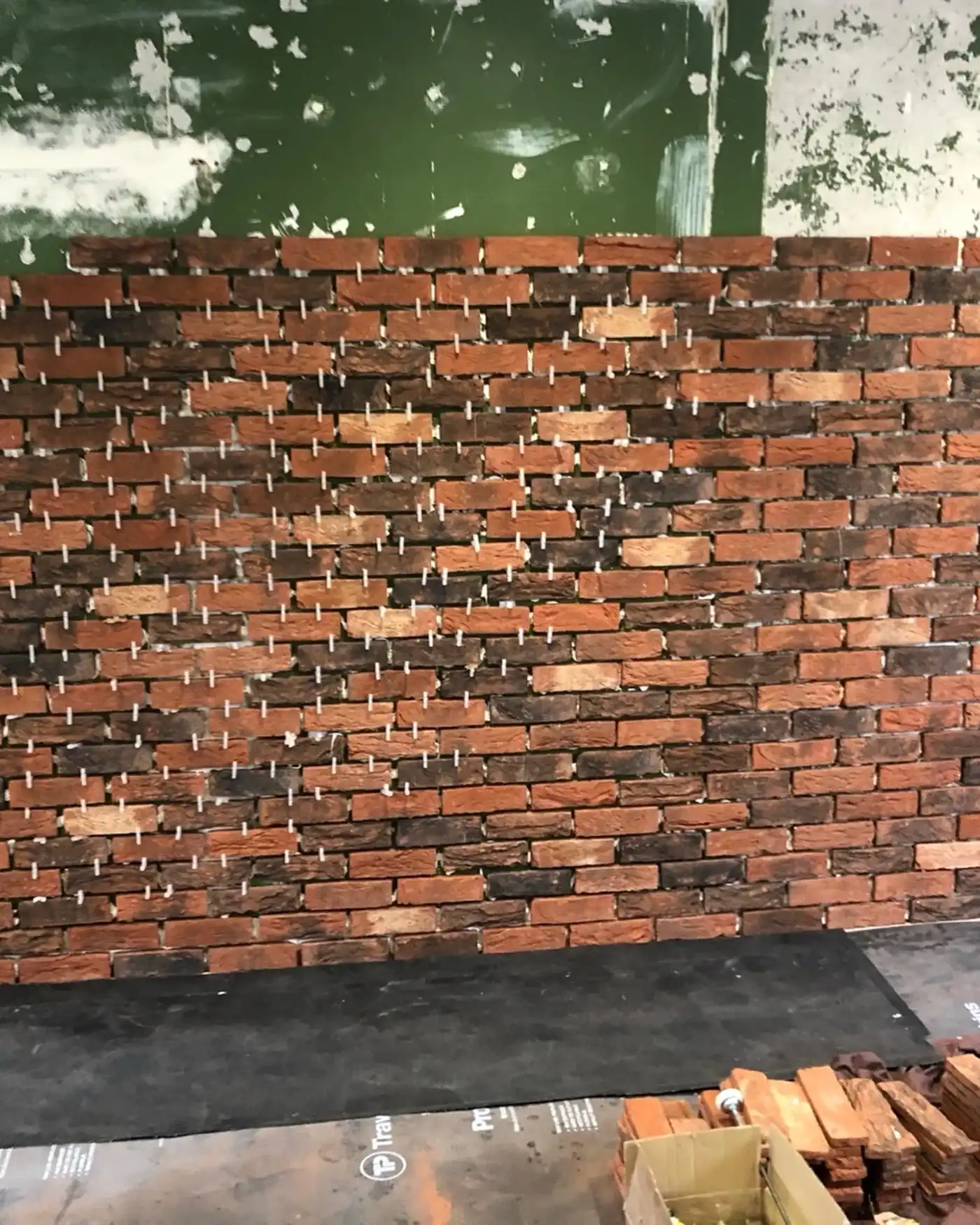 Wall of red bricks partially installed with white spacers on top against a green and white wall.